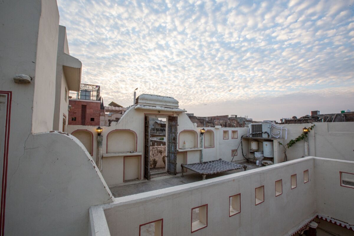 A rooftop terrace with a view of the cityscape, featuring a mix of traditional and modern architecture, including a distinctive white building with a flat roof and a small garden area.