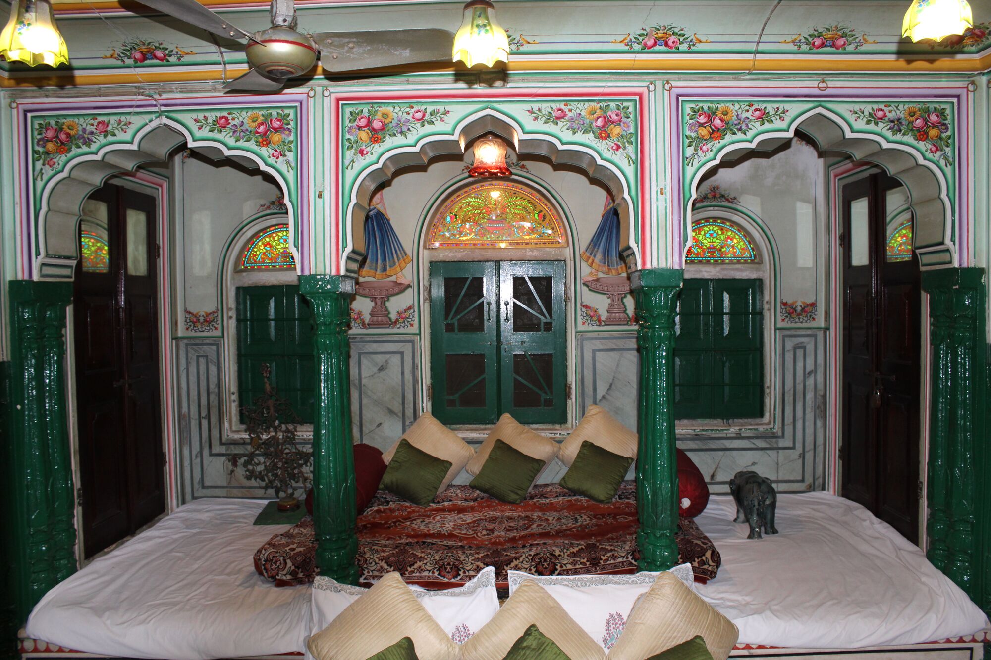 A traditional room with a bed, green pillars, and ornate floral decorations.