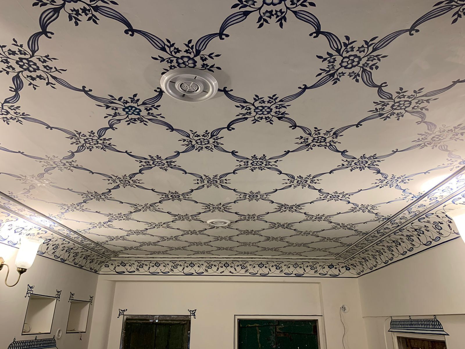 Ein Zimmer mit gemustertem Decken, zwei Fenstern und einer Leuchte.