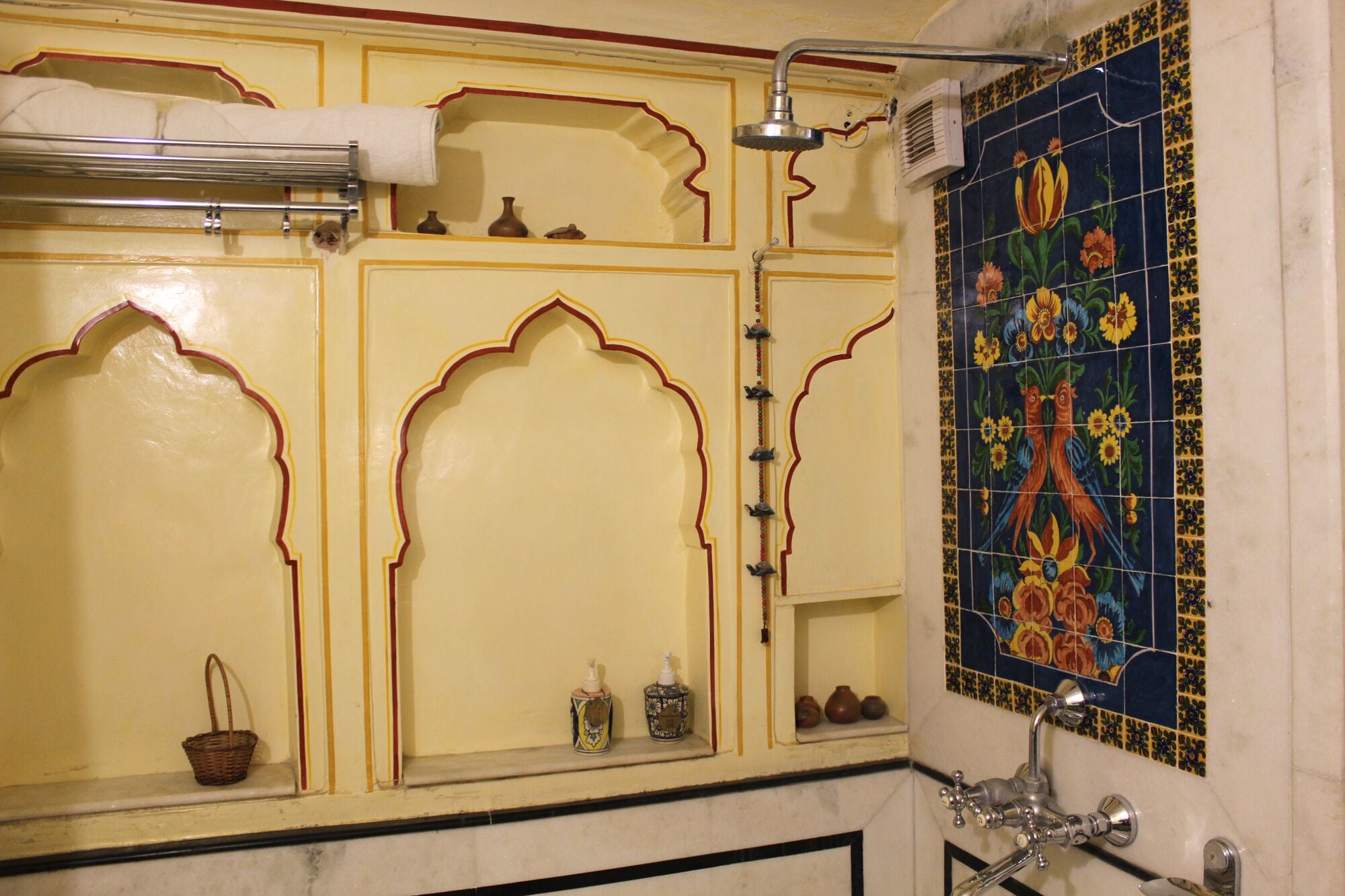 Une salle de bain avec des portes jaunes richement décorées, une douche dotée d’un pommeau de douche à effet pluie et des carreaux décoratifs ornés de motifs floraux.