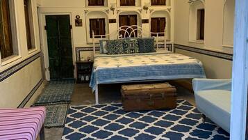 A bedroom with a patterned floor, a bed with a patterned bedspread, a suitcase, a bench, and a door with a green door.