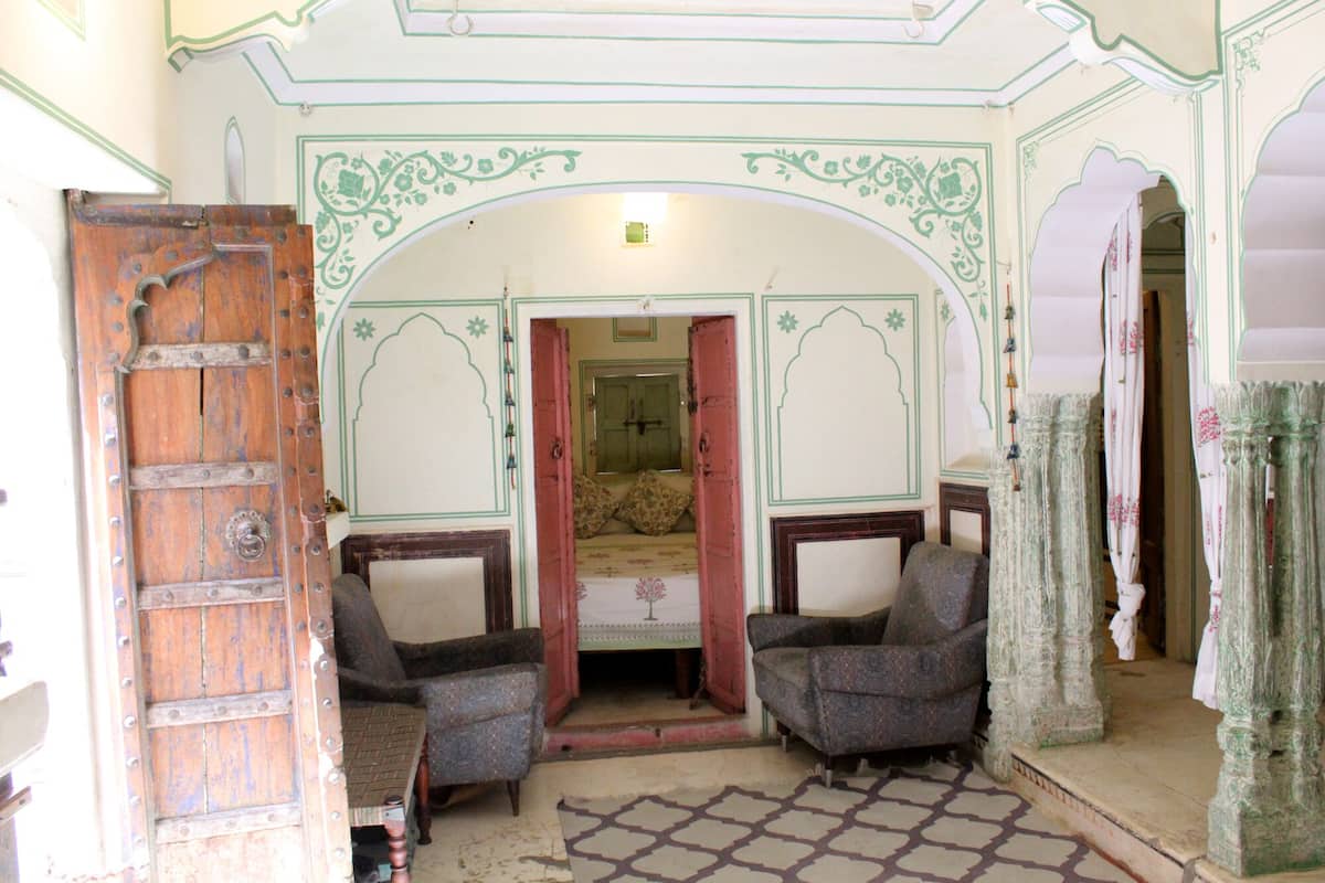 Una habitación con diseño tradicional, que incluye una puerta de madera, dos sillones estampados, un tapete con diseño y un espejo.