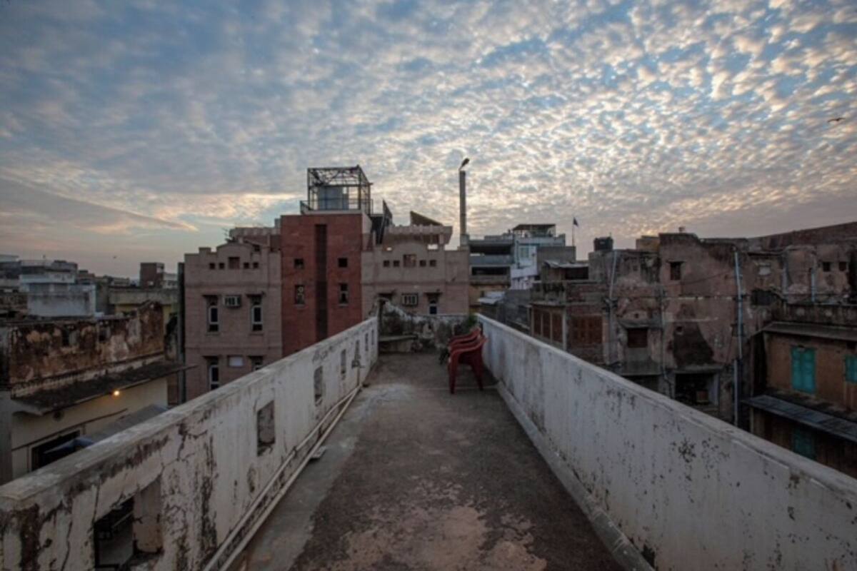 Una azotea con vistas a un paisaje urbano, que incluye una mezcla de edificios residenciales y comerciales, una estructura metálica y una silla roja.