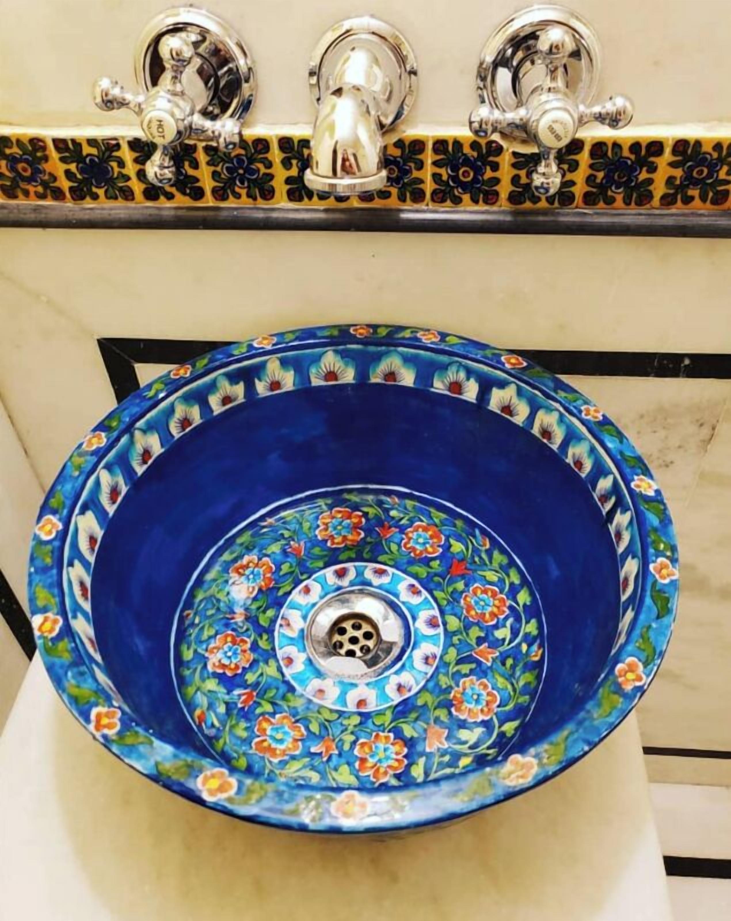 A bathroom sink with a blue basin and floral tile backsplash.