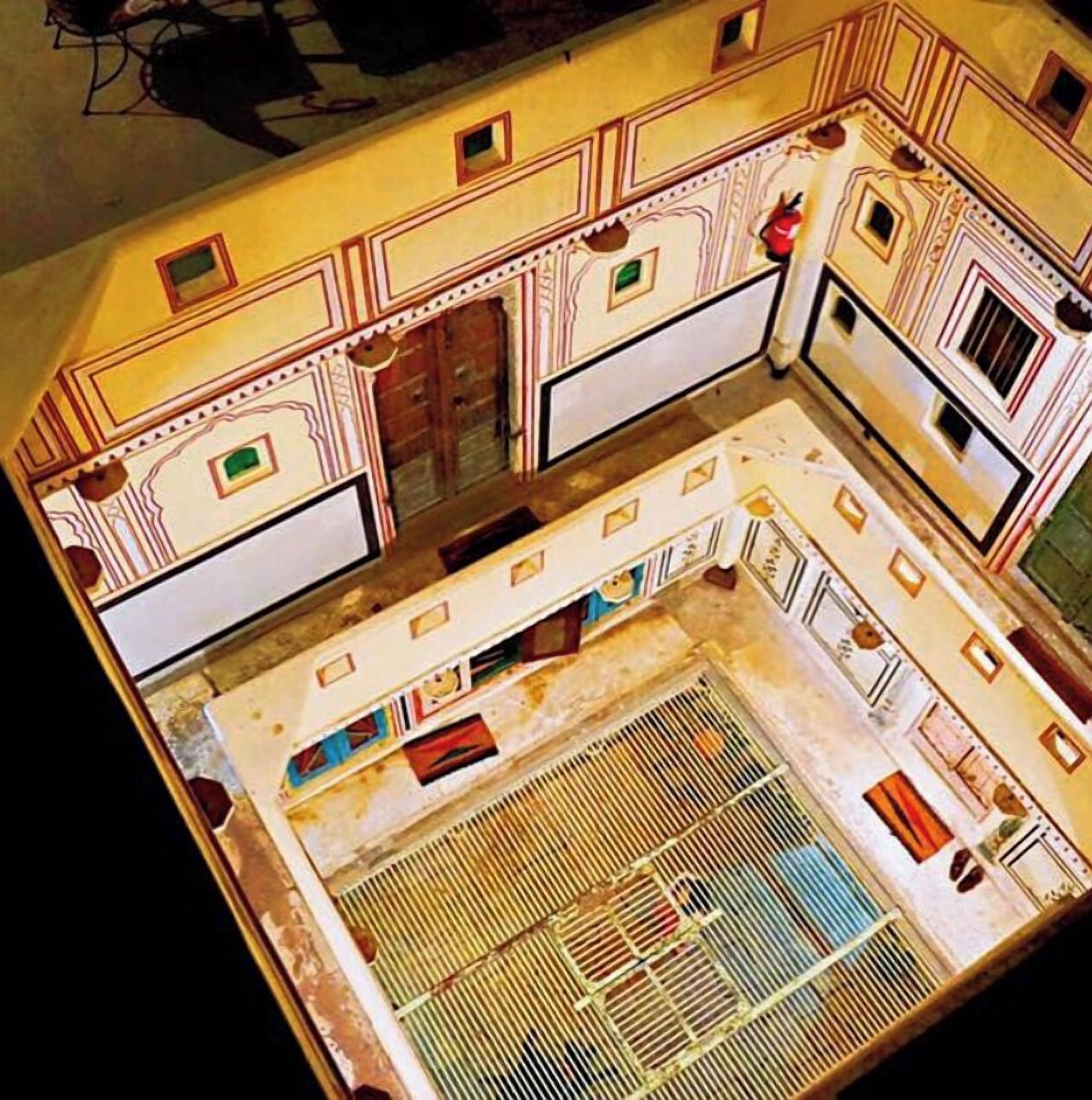Maquete de um espaço central aberto, possivelmente um pátio, rodeado por paredes com desenhos decorativos e pequenas janelas.
