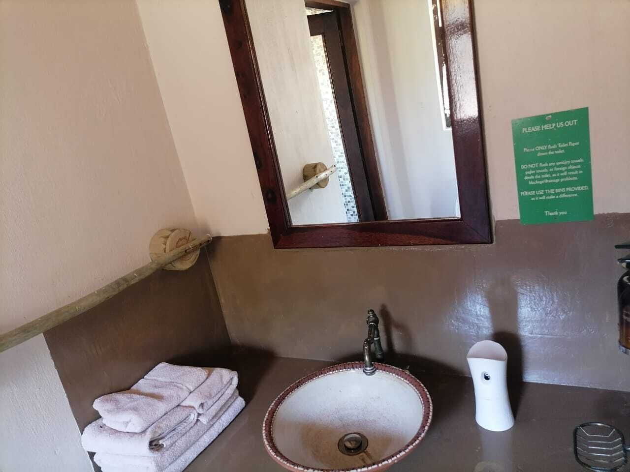 A bathroom with a sink, mirror, and a sign instructing to use the sink provided.