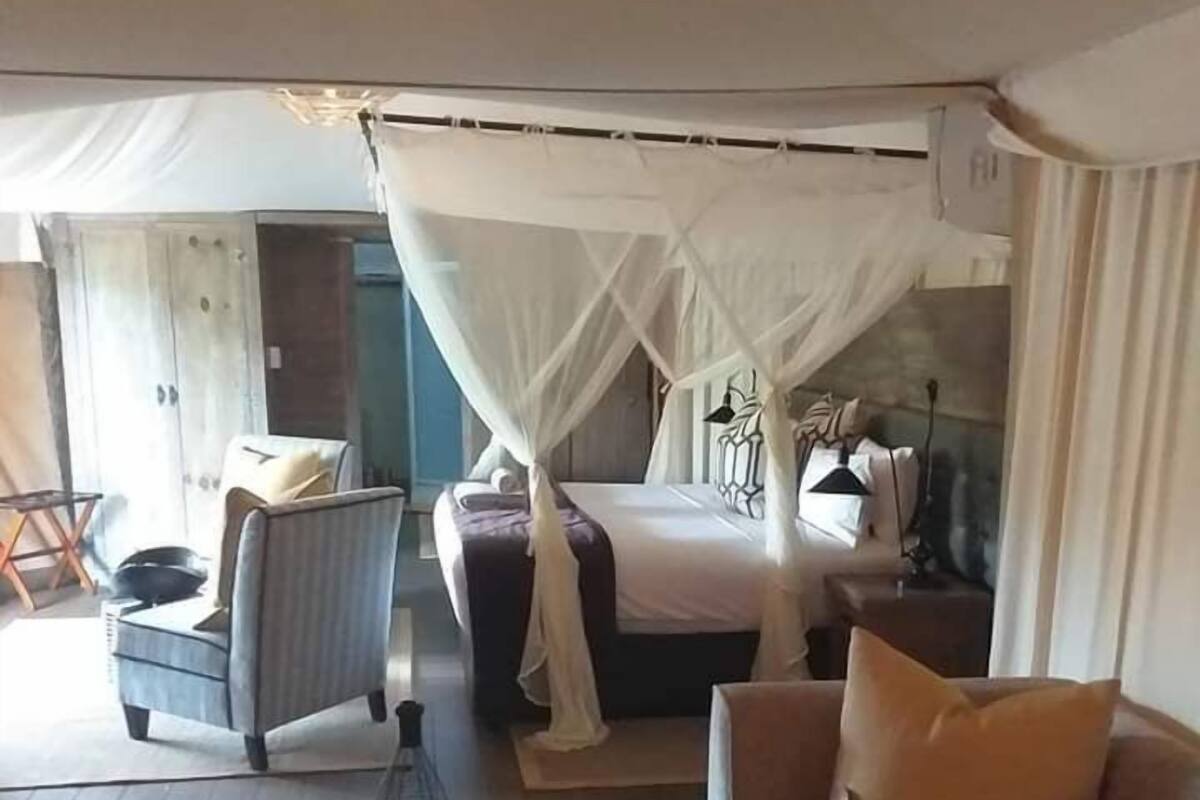 A bedroom with a canopy bed, a sofa, a small table, and a chair.