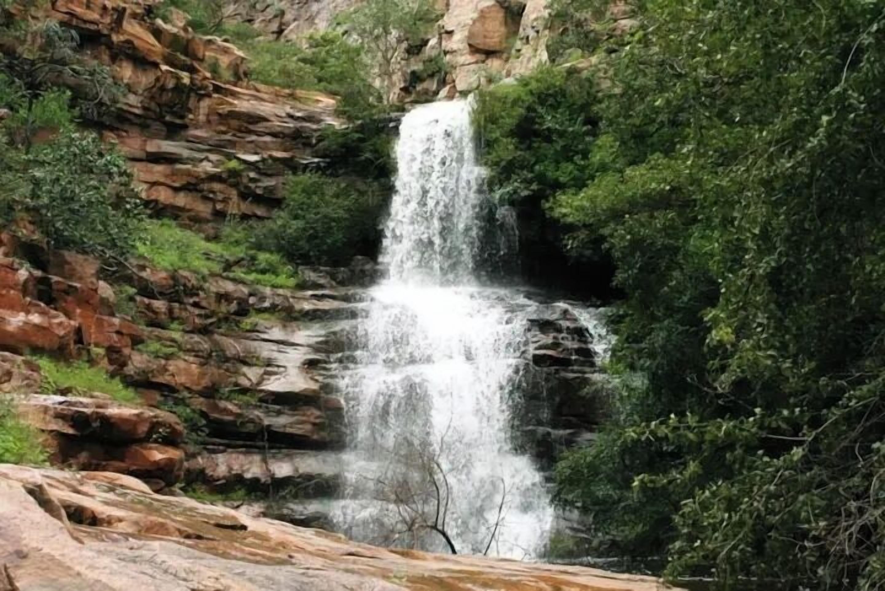 Une cascade se déversant le long d’une falaise rocheuse, entourée d’une végétation luxuriante.