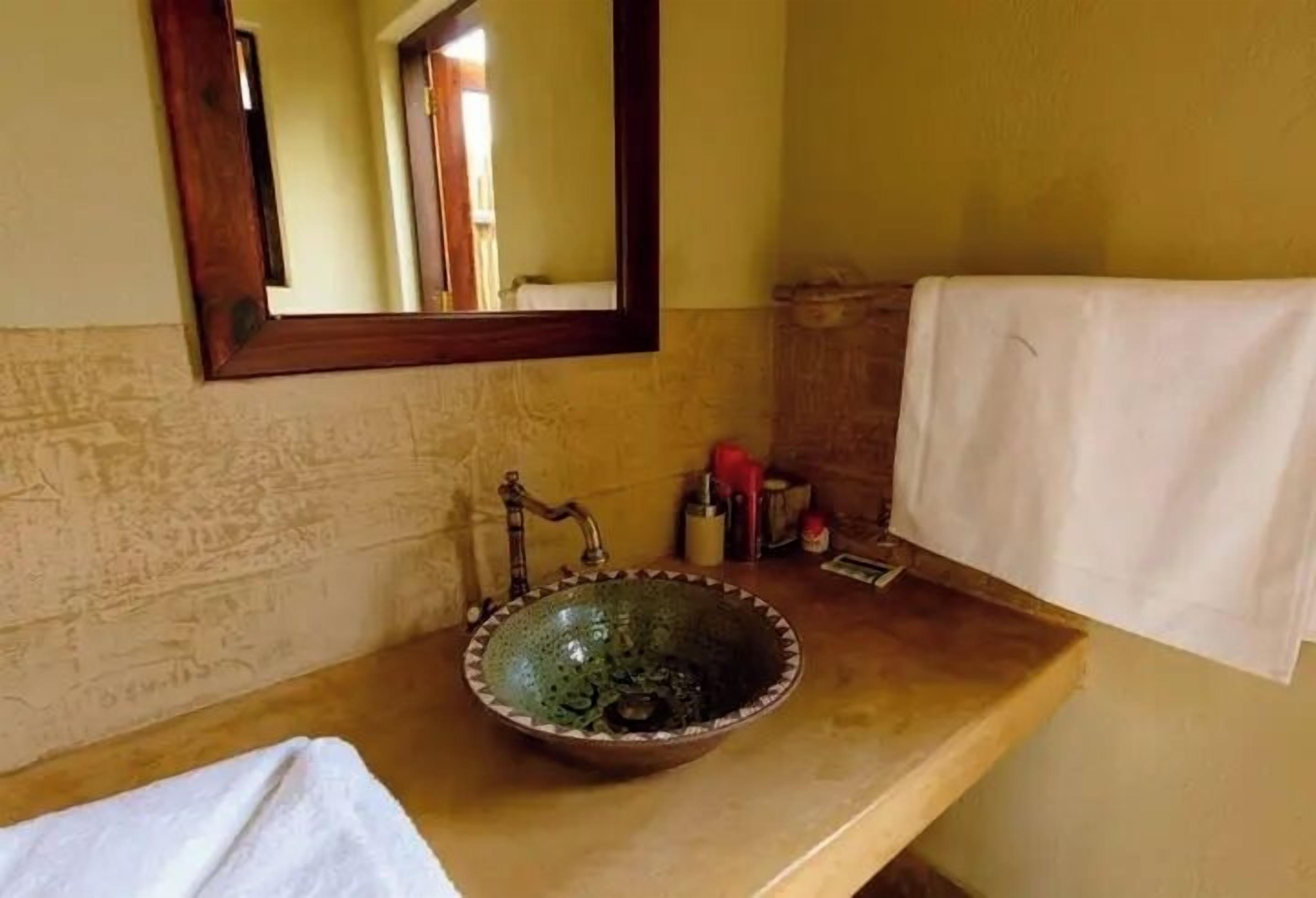 Ein Badezimmer mit einem runden, grünen Keramikwaschbecken, einer Holzauslage, einem Spiegel und einem Handtuch an der Wand.