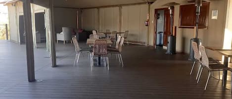 A covered outdoor area with a wooden floor, tables, and chairs arranged for dining or socializing.