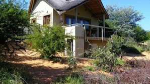 Une maison avec un toit de chaume, un balcon et un chemin de terre menant à l’entrée.