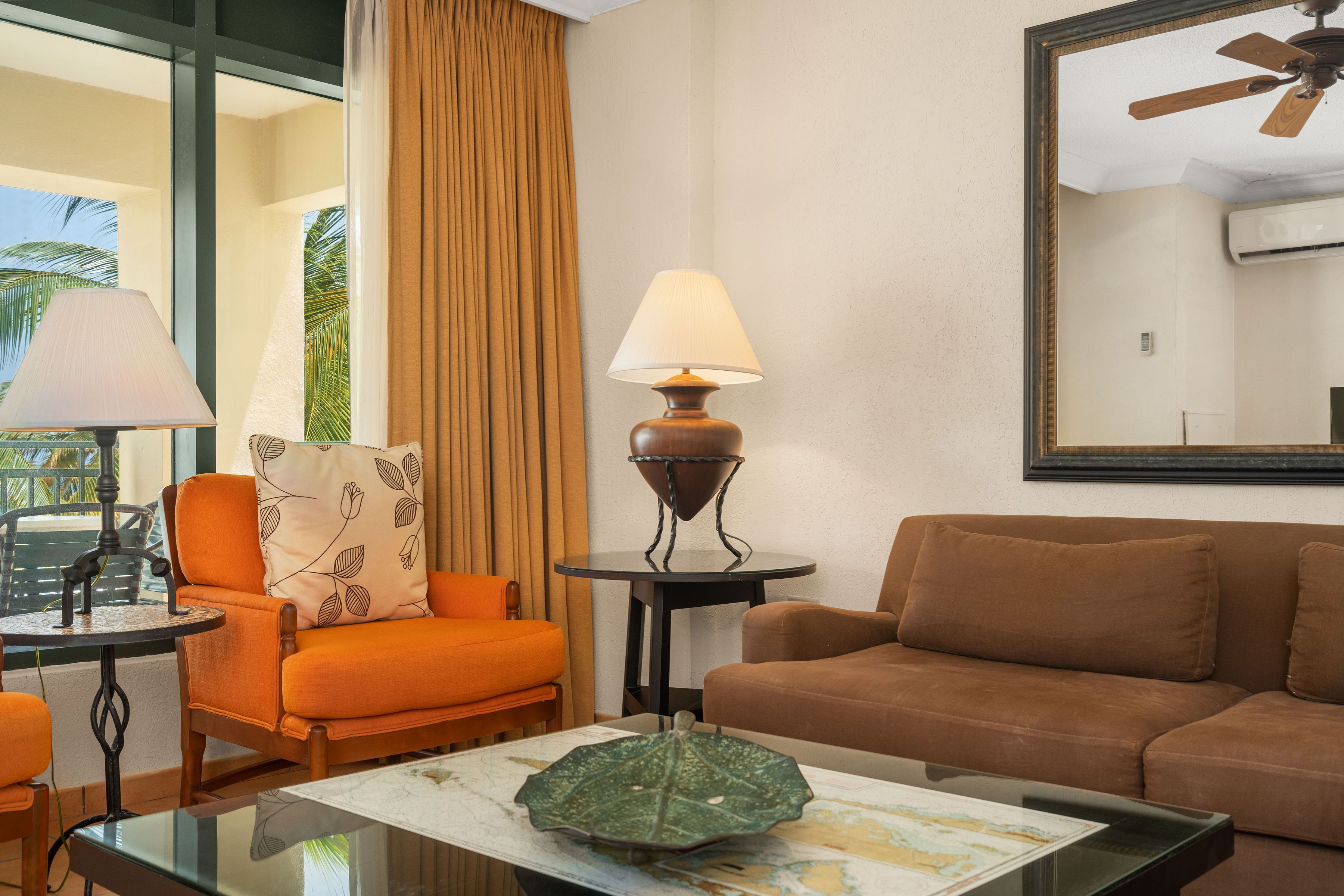 A hotel room with a sofa, armchair, lamp, and a table with a decorative item.