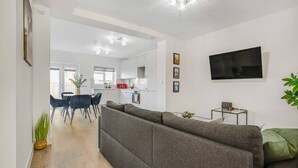 Un salon moderne avec un canapé gris, un téléviseur à écran plat et un coin repas comprenant des chaises et une table.