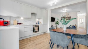 Une cuisine moderne avec des meubles blancs, un micro-ondes rouge et une planche à découper en bois.