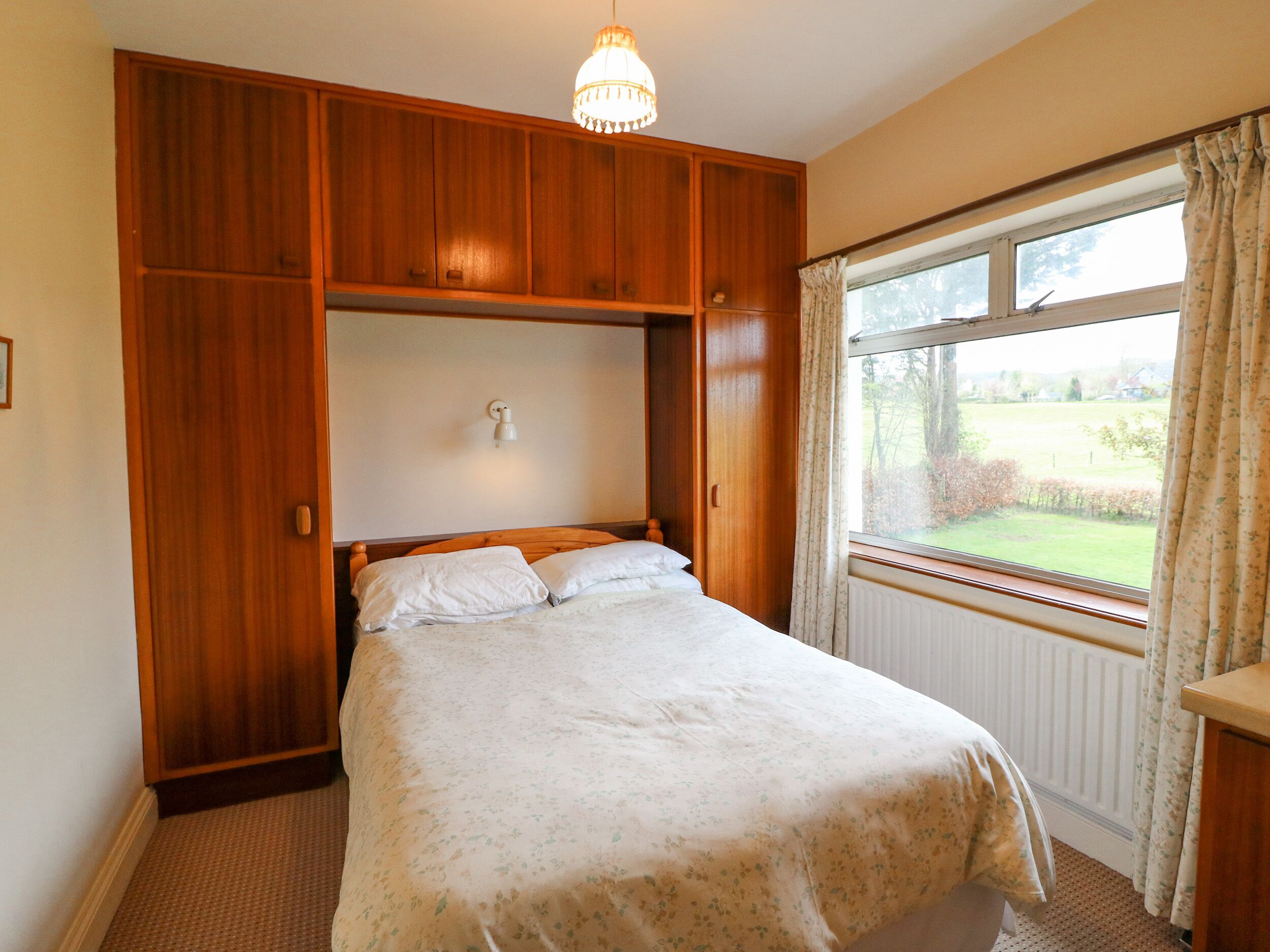 A bedroom with a bed, wooden wardrobe, and a window with curtains.