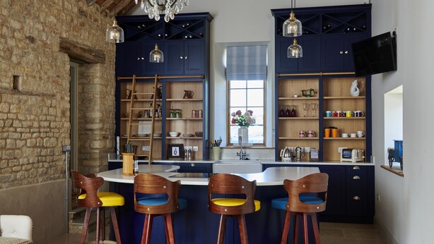 A rustic kitchen with a stone wall, wooden beams, and a large island with bar stools.