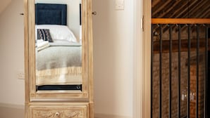 A bedroom with a wooden floor, a bed with white bedding, a wooden-framed mirror, and a sloped ceiling with exposed beams.