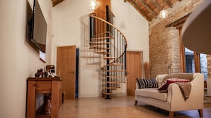 A spacious living room with a wooden staircase, a white sofa, and a television mounted on the wall.