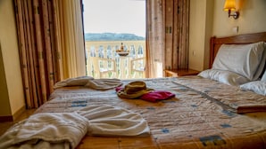 Et hotelværelse med seng, udsigt over et fjerntliggende landskab og en balkon med bord og stole.