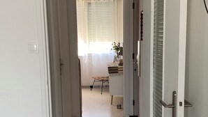 Un corridoio con pareti bianche, pavimento piastrellato e una porta con maniglia metallica.