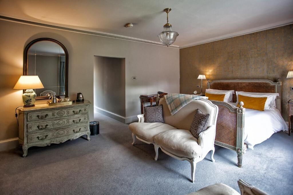 A bedroom with a large bed, a chaise lounge, a dresser, and a mirror.