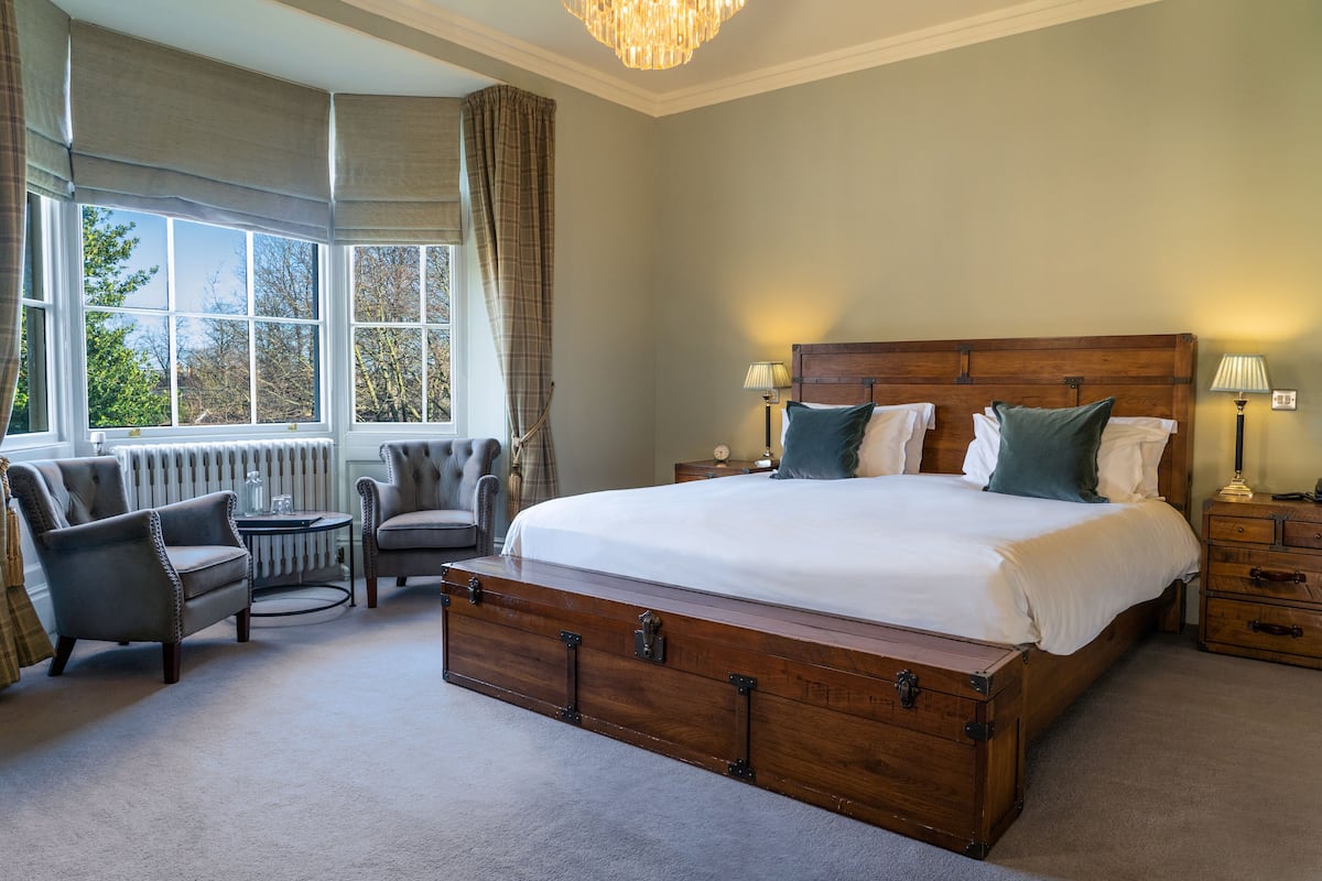 A bedroom with a large wooden bed, two armchairs, a small table, and a nightstand with lamps.