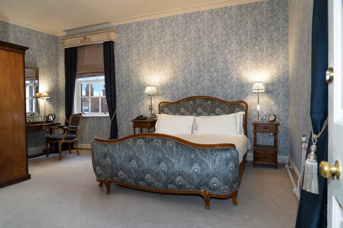 A bedroom with a large bed, two bedside tables with lamps, a dresser, a chair, and a window with curtains.