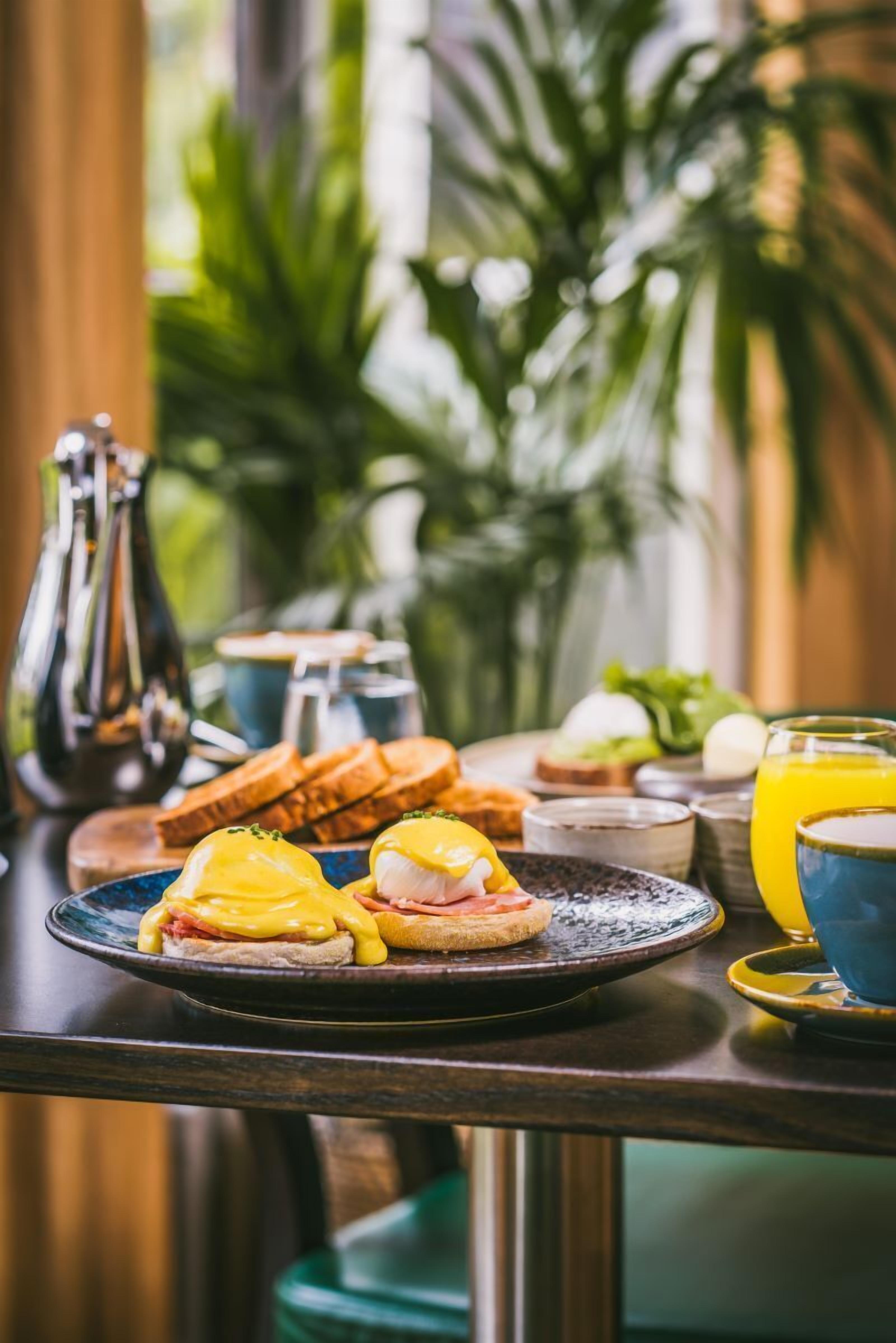 A breakfast table with eggs benedict, toast, and a glass of orange juice.
