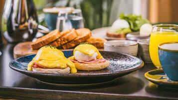 A breakfast table with eggs benedict, toast, and a glass of orange juice.