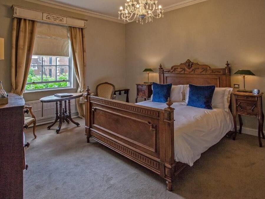 A classic bedroom with a wooden bed, two bedside tables, a chandelier, and a view of greenery outside.