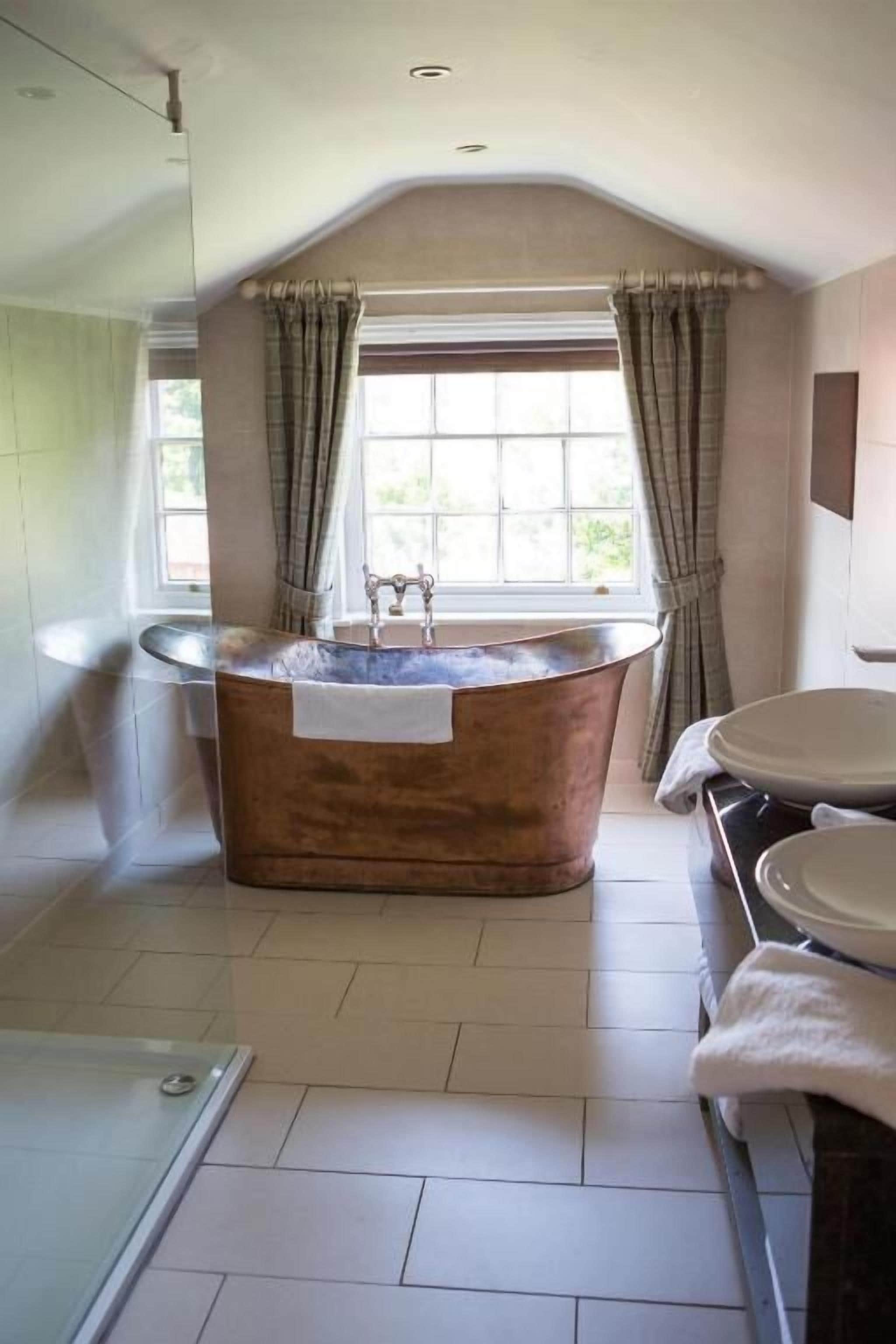 A bathroom with a freestanding copper bathtub, a glass shower enclosure, and a vanity with a sink and mirror.