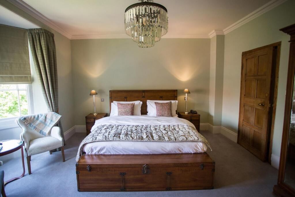 A bedroom with a large bed, two bedside tables, a chandelier, a chair, and a wooden door.