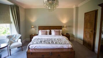 A bedroom with a large bed, two bedside tables, a chandelier, a chair, and a wooden door.