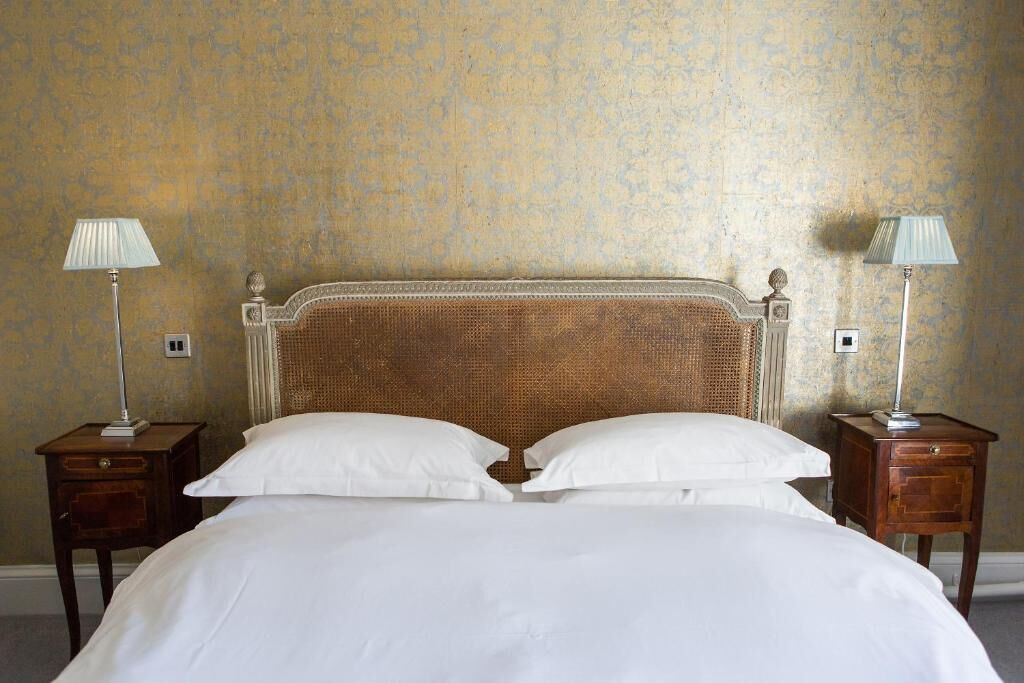 Una cama bien hecha con sábanas blancas, flanqueada por dos mesitas de noche con lámparas, frente a una pared con textura.