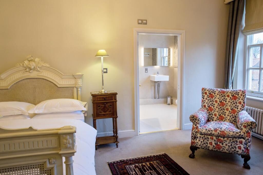A bedroom with a bed, a nightstand, a chair, and a bathroom visible through an open door.