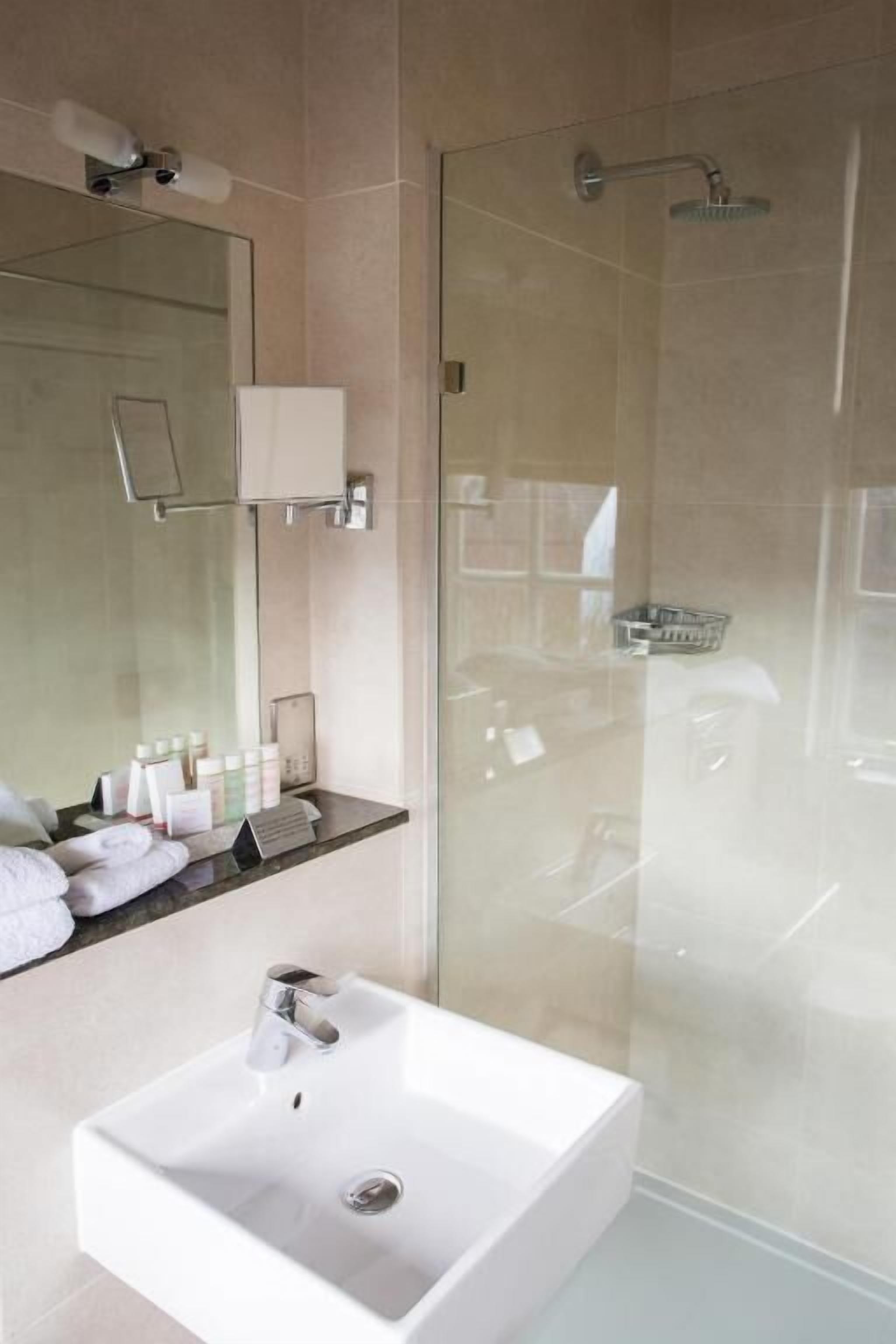 Ein modernes Badezimmer mit einer Duschkabine, einem weißen Waschbecken und einem Spiegel darüber.