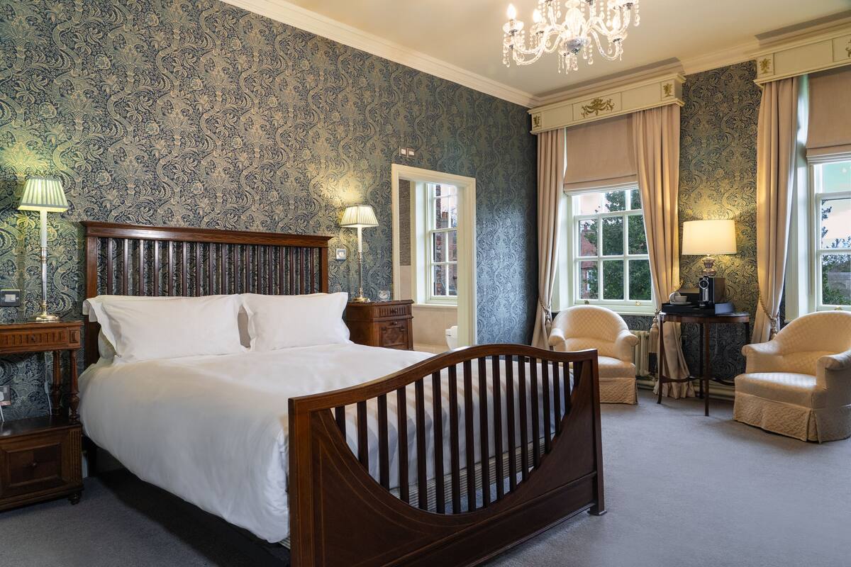 A bedroom with a large bed, two bedside tables, two lamps, a chair, and a window with curtains.