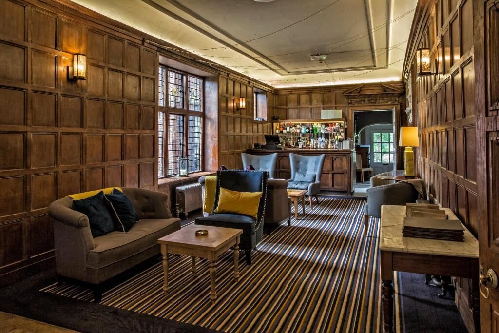 A cozy bar area with wooden paneling, a bar counter, and seating including a sofa and armchairs.
