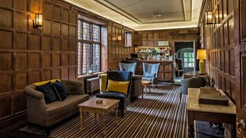A cozy bar area with wooden paneling, a bar counter, and seating including a sofa and armchairs.