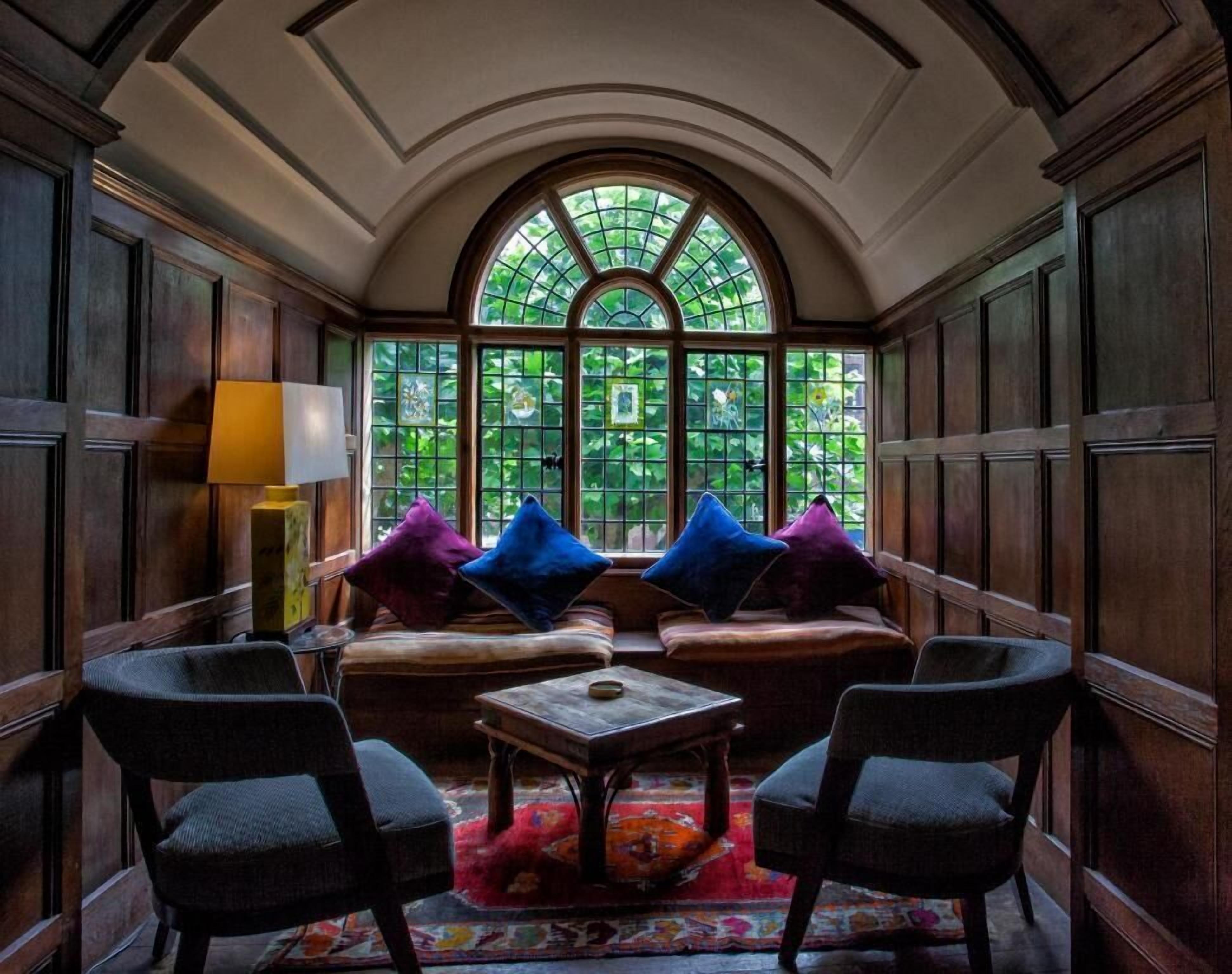 A cozy room with a wooden bench, two armchairs, a small table, and a colorful rug.