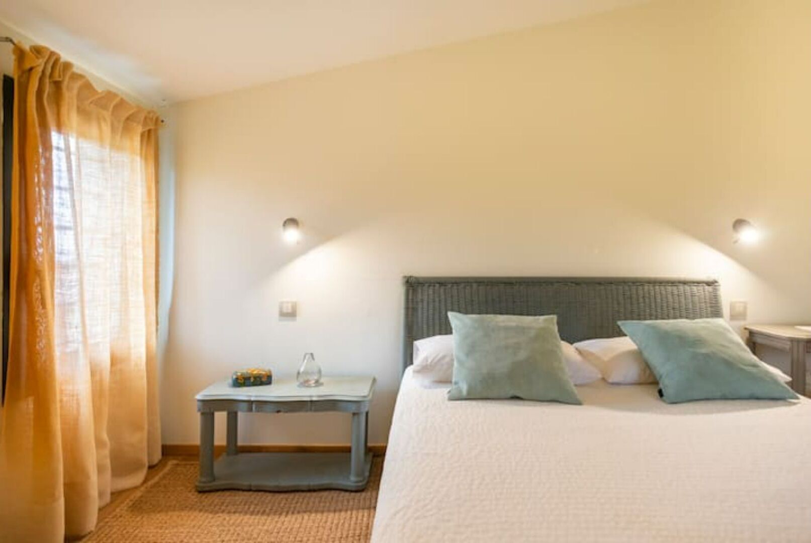 A bedroom with a bed, two bedside tables, a nightstand, and a window with curtains.