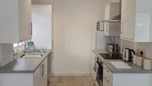 Pieni, käytännöllinen keittiö, jossa on valkoiset kaapit, pesuallas, mikroaaltouuni ja vedenkeitin.