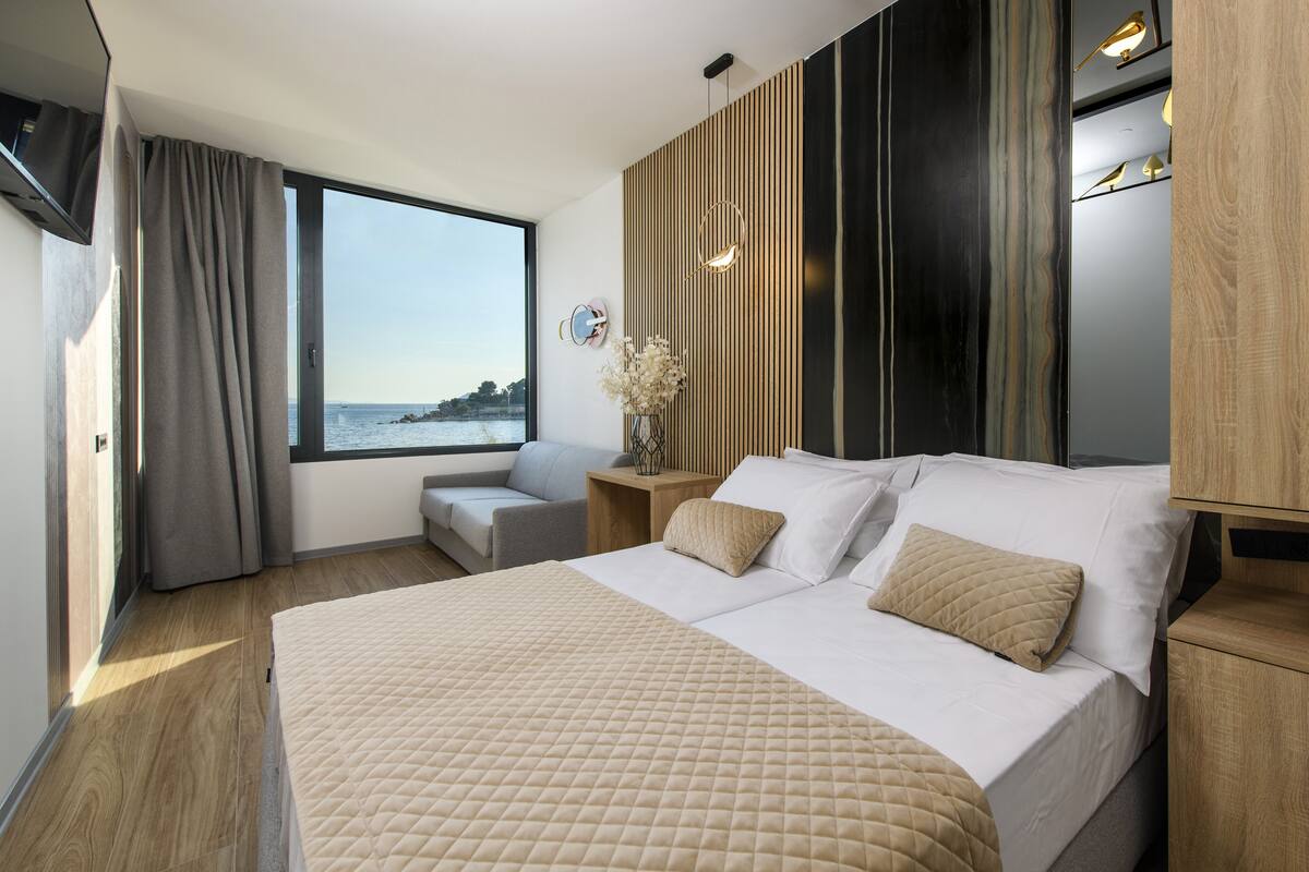 Habitación de hotel moderna con una cama grande, vistas al mar y una pared de madera decorativa.