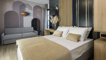 A modern bedroom with a large bed, a grey sofa, and a wooden nightstand with a vase of flowers.