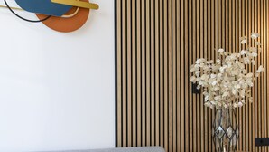 A modern living room with a grey sofa, a wooden slatted wall, and a decorative vase with dried flowers on a wooden console table.