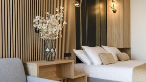 A modern bedroom with a wooden slat wall, a bedside table with a vase of flowers, a bed with white bedding, and a grey sofa.