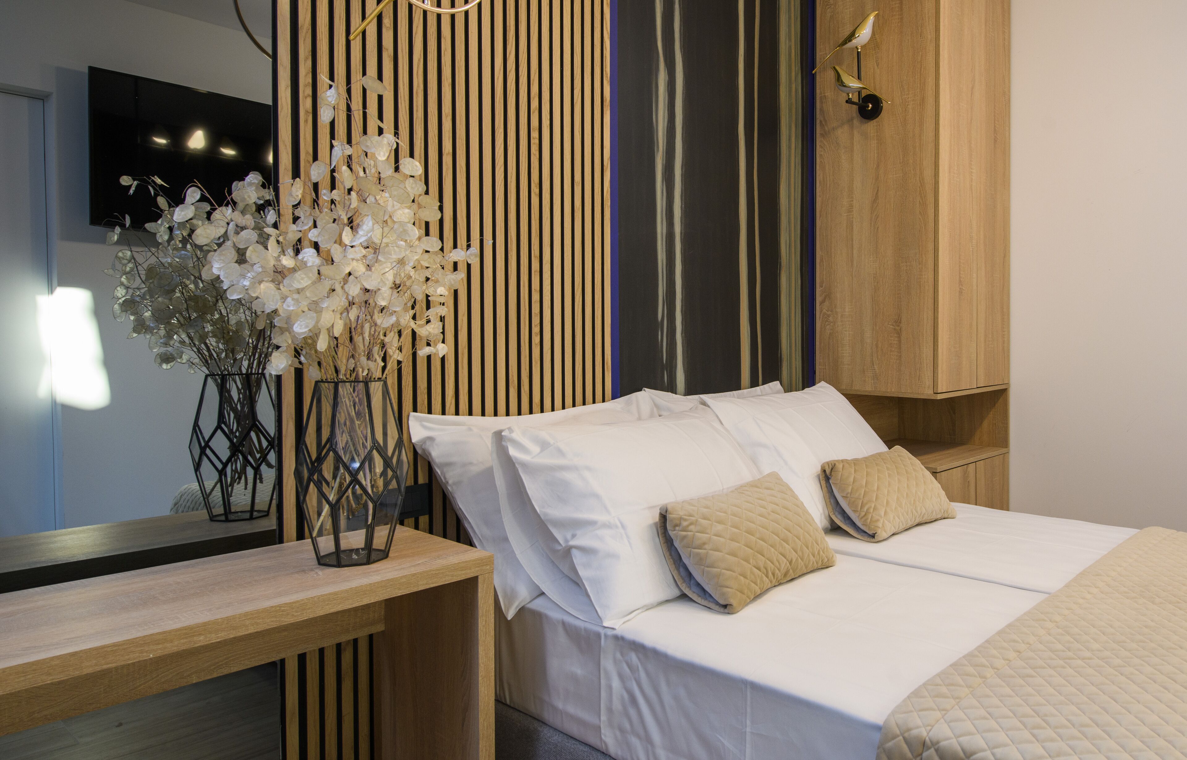 A modern bedroom with a bed, bedside tables, a TV, and a decorative plant.
