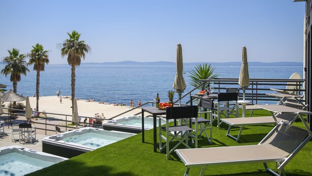 A rooftop pool area with lounge chairs, a hot tub, and a view of the beach and sea.