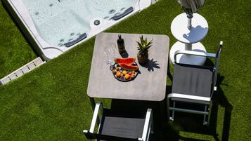 Un jacuzzi rodeado por un césped, una mesa con frutas y bebidas, y dos sillas.