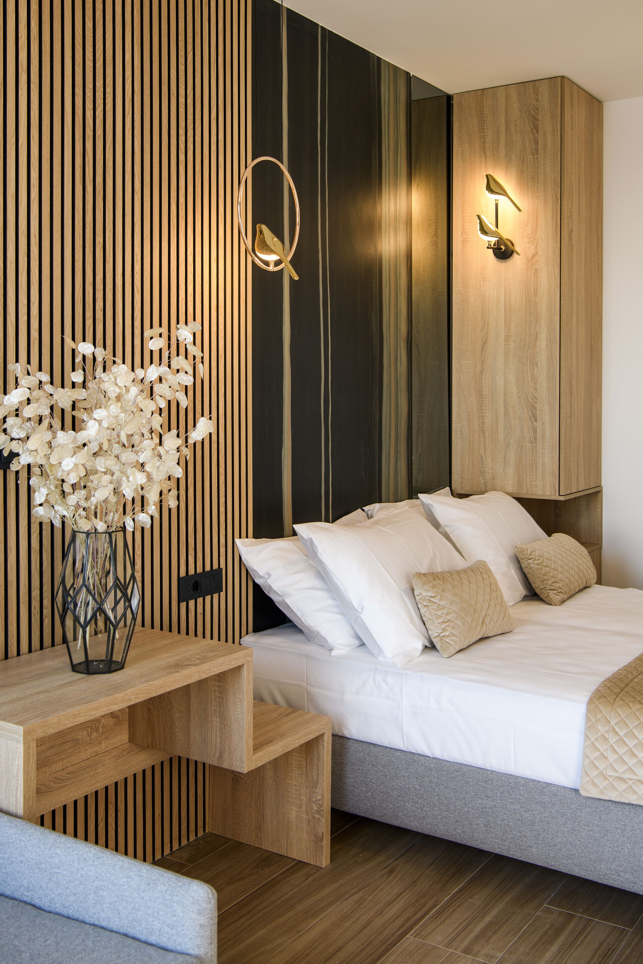A modern bedroom with a bed, bedside lamps, a wooden desk, and a vase of flowers.